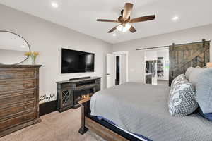 Bedroom featuring a barn door, light carpet, recessed lighting, a walk in closet, and ceiling fan