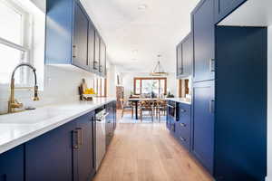 Kitchen with blue cabinetry, light wood-style flooring, light countertops, and a chandelier