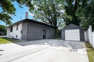 View of home's exterior featuring a garage, a chimney, an outbuilding, and concrete driveway