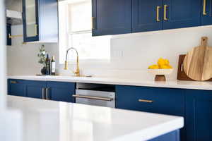 Kitchen featuring blue cabinets, light countertops, glass insert cabinets, and dishwasher