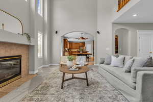 Living area featuring a ceiling fan, arched walkways, a tile fireplace, a high ceiling, and light carpet