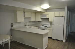 Kitchen with white appliances, a peninsula, light countertops, dark wood finished floors, and white cabinets