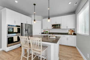 Kitchen featuring dark countertops, appliances with stainless steel finishes, tasteful backsplash, light wood finished floors, and white cabinets