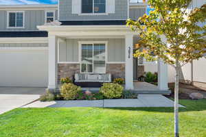 Entrance to property with board and batten siding, a porch, roof with shingles, and stone siding