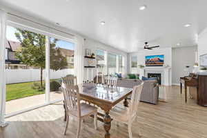 Dining area featuring a warm lit fireplace, a ceiling fan, light wood-style floors, recessed lighting, and a textured ceiling