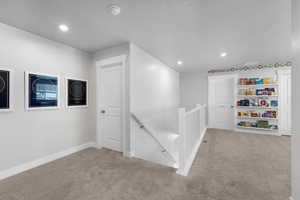 Hallway with an upstairs landing, carpet, recessed lighting, built in features, and a textured ceiling