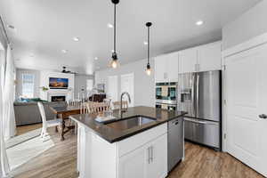 Kitchen with dark countertops, appliances with stainless steel finishes, light wood-style floors, a lit fireplace, and a ceiling fan