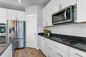 Kitchen with appliances with stainless steel finishes, dark countertops, decorative backsplash, light wood-style flooring, and white cabinets