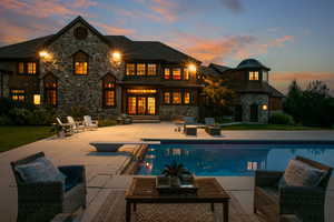 Rear view of house with stone siding, an outdoor pool, a patio, and a lawn