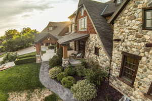 Back of house featuring stone siding, roof with shingles, a garage, a lawn, and covered porch