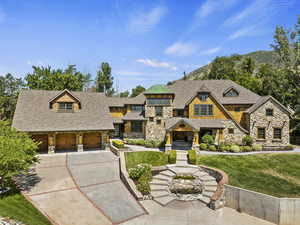 Shingle-style home with stone siding, a garage, concrete driveway, and a front lawn
