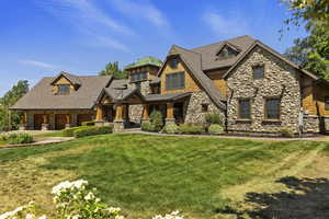 Shingle-style home featuring stone siding, a front lawn, and covered porch