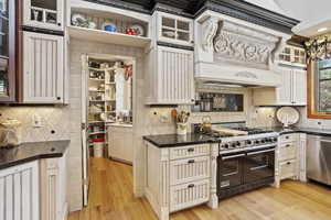 Kitchen with stainless steel appliances, tasteful backsplash, light wood finished floors, custom range hood, and glass insert cabinets