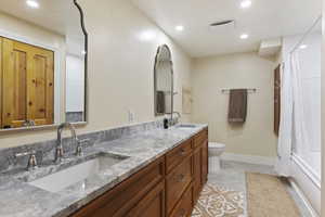 Full bathroom with double vanity, recessed lighting, toilet, shower / bath combination with curtain, and baseboards
