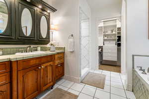 Full bathroom featuring vanity, light tile patterned flooring, a bath, and a walk in closet