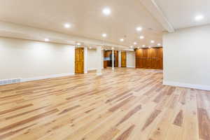 Finished below grade area with recessed lighting, light wood-type flooring, and black fridge with ice dispenser
