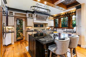 Kitchen with backsplash, light wood-type flooring, beam ceiling, a center island, and glass insert cabinets