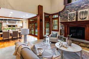 Living room featuring recessed lighting, a stone fireplace, light wood-type flooring, a high ceiling, and french doors