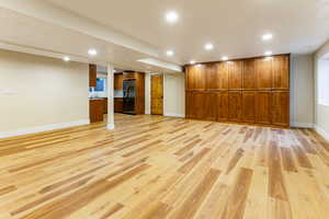 Finished below grade area featuring recessed lighting, light wood finished floors, and stainless steel fridge