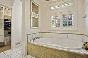 Full bath featuring a garden tub, tile patterned floors, a walk in closet, and baseboards