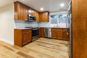 Kitchen featuring brown cabinetry, light stone counters, appliances with stainless steel finishes, light wood-style floors, and decorative backsplash