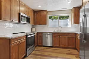 Kitchen featuring appliances with stainless steel finishes, a sink, brown cabinets, a textured ceiling, and recessed lighting