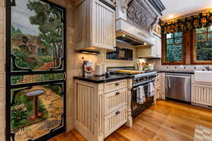 Kitchen with light wood-style floors, luxury range, dishwasher, premium range hood, and tasteful backsplash
