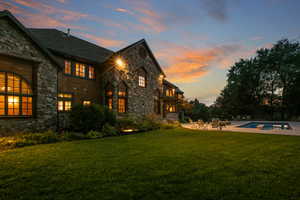 Back of house at dusk with stone siding, a yard, an outdoor pool, and a patio