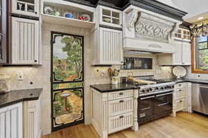 Kitchen featuring appliances with stainless steel finishes, decorative backsplash, light wood finished floors, glass insert cabinets, and cream cabinets