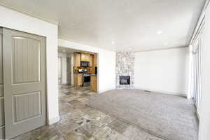 Unfurnished living room featuring a textured ceiling, stone tile floors, a stone fireplace, recessed lighting, and ornamental molding