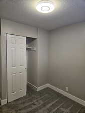Unfurnished bedroom with dark colored carpet, a closet, and a textured ceiling