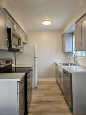Kitchen with stainless steel appliances, light wood-type flooring, sink, and gray cabinetry