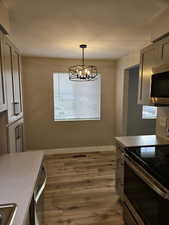 Kitchen with an inviting chandelier, dark wood-type flooring, stainless steel appliances, hanging light fixtures, and gray cabinetry