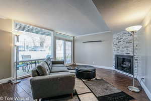 Living area with expansive windows, a textured ceiling, a stone fireplace, and wood finished floors
