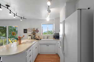 Kitchen with white refrigerator with ice dispenser, light countertops, light wood-type flooring, a peninsula, and white cabinetry