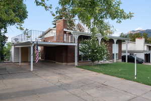 View of front facade featuring driveway, brick siding, a chimney, and an attached carport