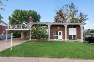 View of front of property featuring a front yard, driveway, brick siding, a chimney, and a carport
