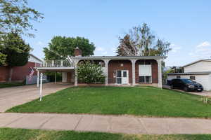View of front of property featuring brick siding, concrete driveway, a front lawn, and a chimney