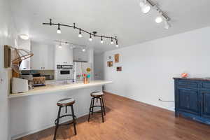 Kitchen featuring a peninsula, track lighting, light wood-type flooring, white appliances, and a breakfast bar area
