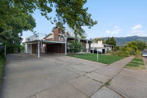 View of front facade with brick siding, driveway, a mountain view, a front lawn, and a chimney