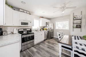 Kitchen with appliances with stainless steel finishes, backsplash, white cabinetry, wood finished floors, and ceiling fan