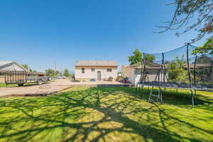 Rear view of house with a trampoline, a lawn, an outbuilding, and a patio