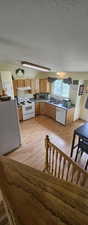Kitchen featuring appliances with stainless steel finishes, a textured ceiling, light wood finished floors, brown cabinets, and under cabinet range hood