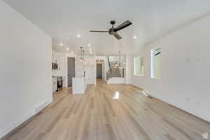 Unfurnished living room with light wood-style flooring, stairway, ceiling fan, recessed lighting, and a chandelier