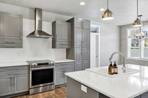 Kitchen with gray cabinetry, electric stove, wall chimney exhaust hood, backsplash, and recessed lighting