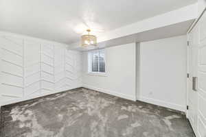 Carpeted empty room featuring baseboards and a chandelier