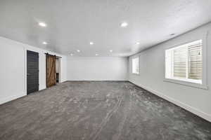Empty room featuring a barn door, dark carpet, a textured ceiling, and recessed lighting