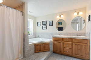 Full bath featuring a textured ceiling, double vanity, a bath, tile patterned flooring, and curtained shower
