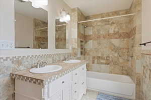 Bathroom with tile walls, decorative backsplash, double vanity, and washtub / shower combination