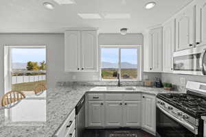 Kitchen featuring appliances with stainless steel finishes, a mountain view, white cabinetry, recessed lighting, and granite countertops